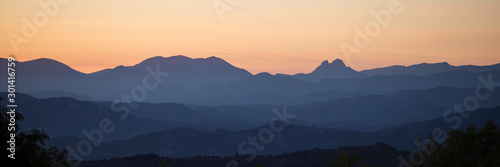 Panoramic silhouette of mountains against an orange sky.