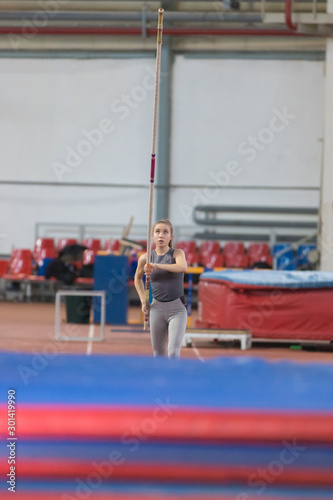 Pole vaulting indoors - young sportive woman running with a pole in the hands - looking up at the pole before jumping