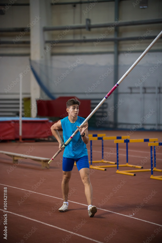 Pole vaulting indoors - young man standing on the runway holding a pole
