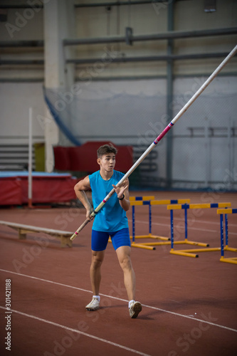 Pole vaulting indoors - young man standing on the runway holding a pole © KONSTANTIN SHISHKIN