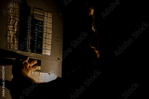 Man Checks Home Fuse Box in a Dark Power Outage