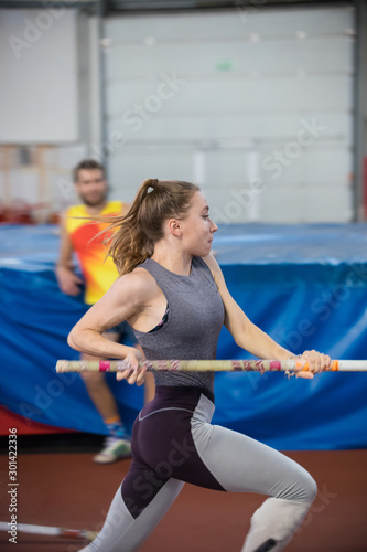 Pole vaulting indoors - young sportive woman with ponytail running with a pole in the hands
