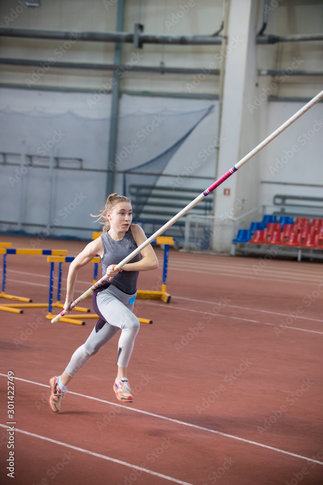 Pole vaulting indoors - young woman in leggins running with a pole in the hands