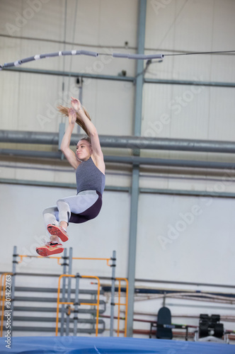 Pole vaulting indoors - young sportive woman with a ponytail falling down after the jump