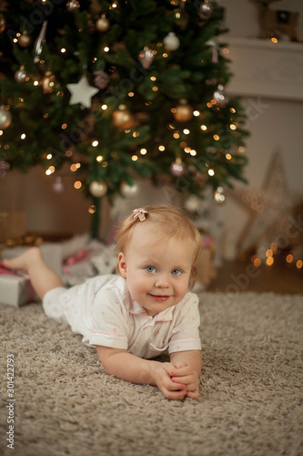 Little cute girl of 2 years in pajamas opens gifts at the Christmas tree. Christmas. New Year. Holidays. Cozy.