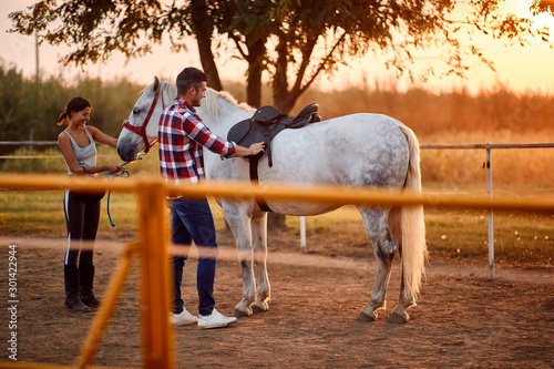 Woman rider getting horse ready for ride at sunset