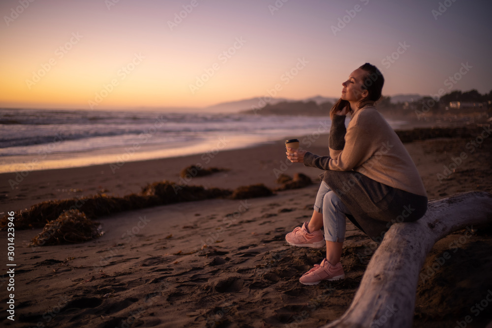 Fototapeta premium Woman enjoying hot drink on a sunset near ocean