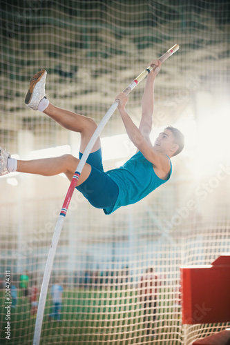 Vászonkép Pole vaulting indoors - young fit man jumping leaning on the pole - sport stadiu