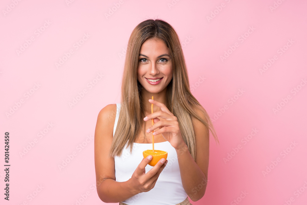 Young blonde woman over isolated background holding an orange Young blonde woman over isolated background holding an orange