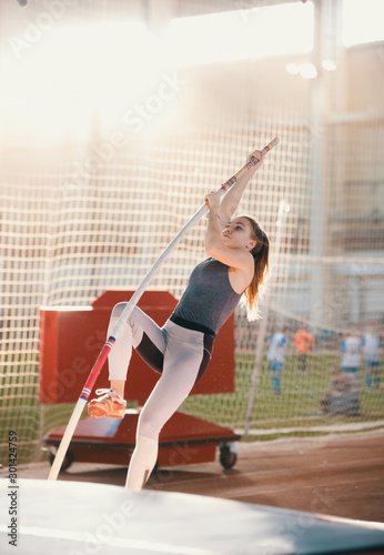 Slika na platnu Pole vaulting indoors - young sportive woman with a ponytail leaning on the pole