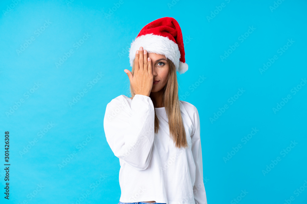 Girl with christmas hat over isolated background covering a eye by hand Girl with christmas hat over isolated background covering a eye by hand