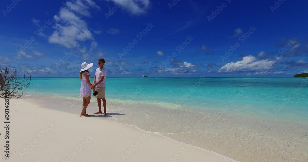 Young couple dressed on white standing on shallow water of tropical bay, whispering to each other, holidays in Bali Young couple dressed on white standing on shallow water of tropical bay, whispering to each other, holidays in Bali