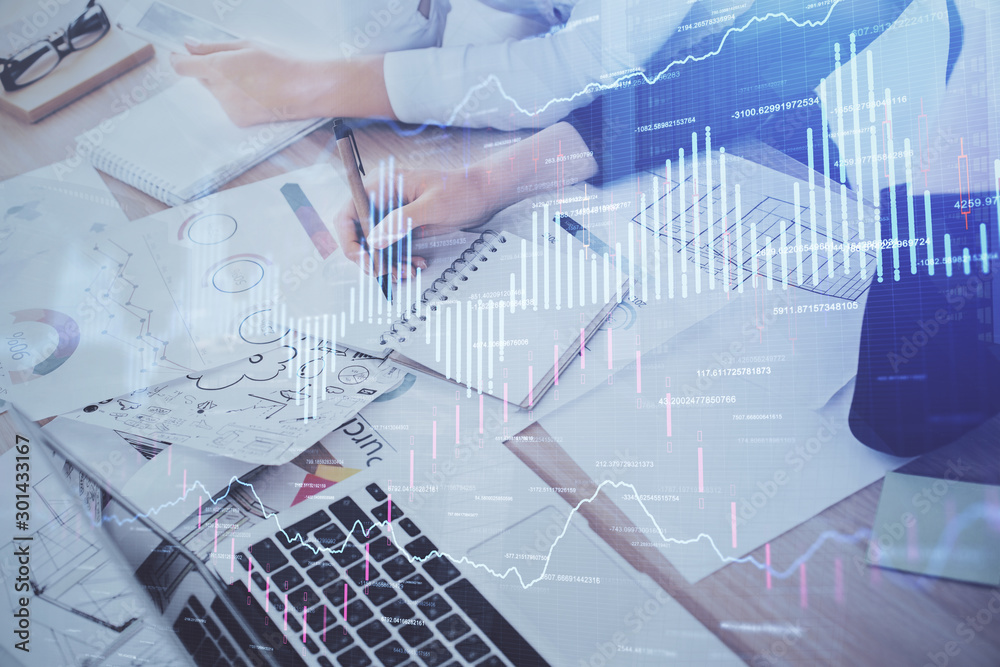 A woman hands writing information about stock market in notepad. Forex chart holograms in front. Concept of research. Double exposure A woman hands writing information about stock market in notepad. Forex chart holograms in front. Concept of research. Double exposure