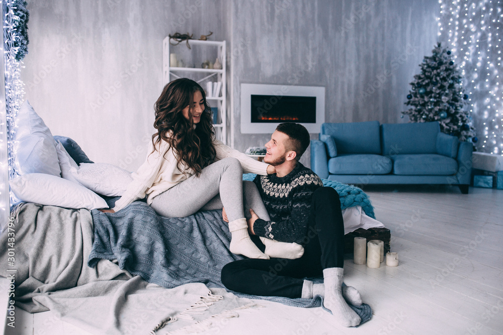 Naklejka premium A guy with a girl is celebrating Christmas. A loving couple enjoys each other on New Year's Eve in a cozy home environment. New Year's love story.