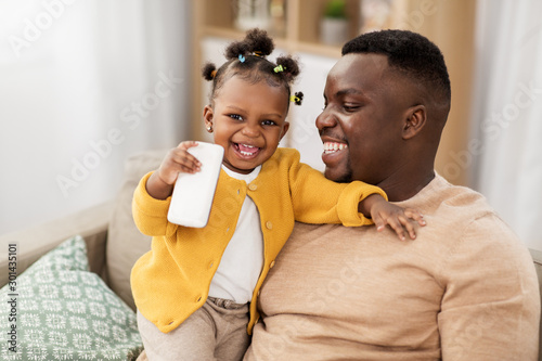 family, fatherhood and technology concept - african american father and little baby daughter with smartphone at home