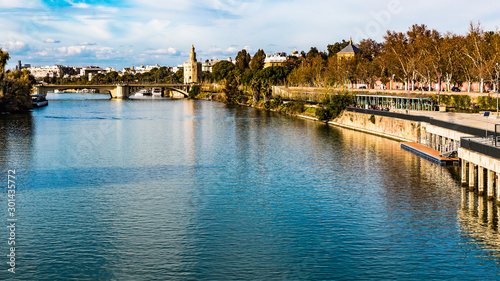 Guadalquivir river with reflection with a bridge and the Golden Tower in the background  sunny day with a blue sky in the city of Seville  Spain