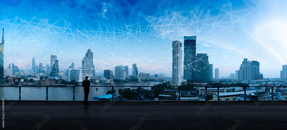 Businessman standing using smart phone in modern space watching city night view.Business Wireless network and Connection technology concept. - obrazy, fototapety, plakaty 