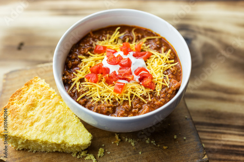 Overhead view of a bowl of red chili and piece of cornbread. 