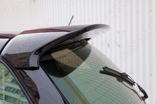 View of the trunk lid of a black car with a plastic spoiler over the rear window to improve the aerodynamics of the vehicle body during tuning for racing.