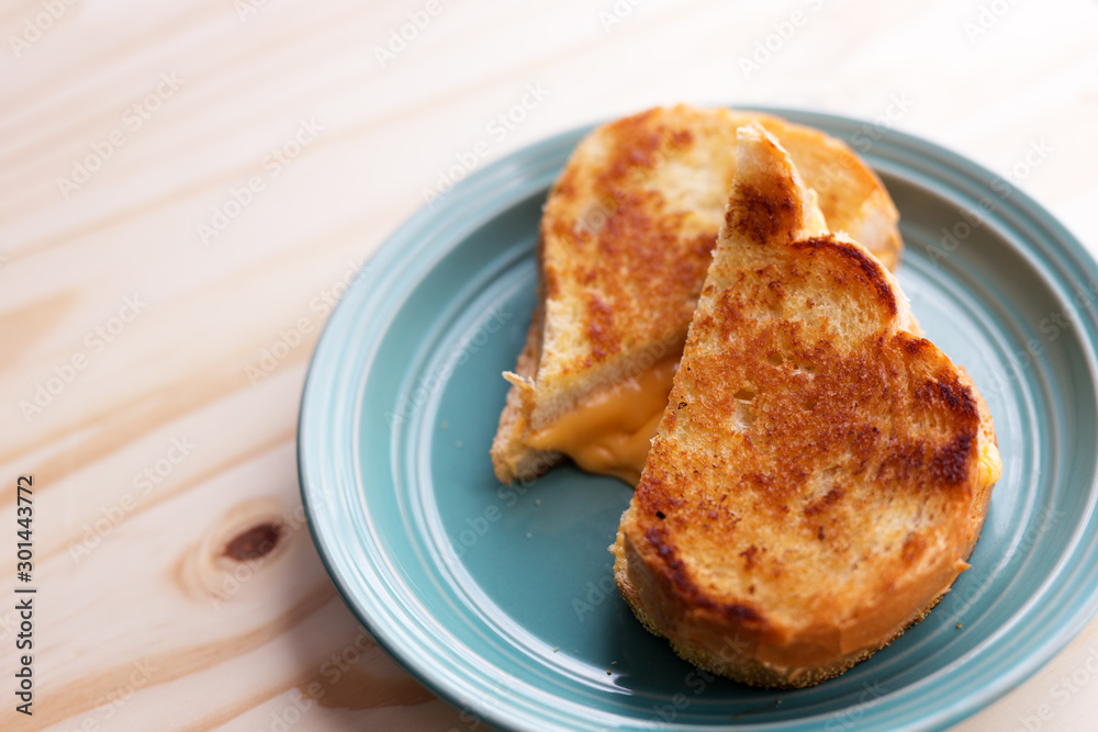 Whole grilled cheese sandwich, cut in half on a blue plate and wooden table. Whole grilled cheese sandwich, cut in half on a blue plate and wooden table.