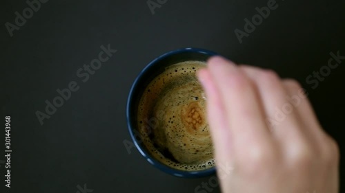 Espresso coffee cup top view with woman hand stirring in the coffee cup on black background