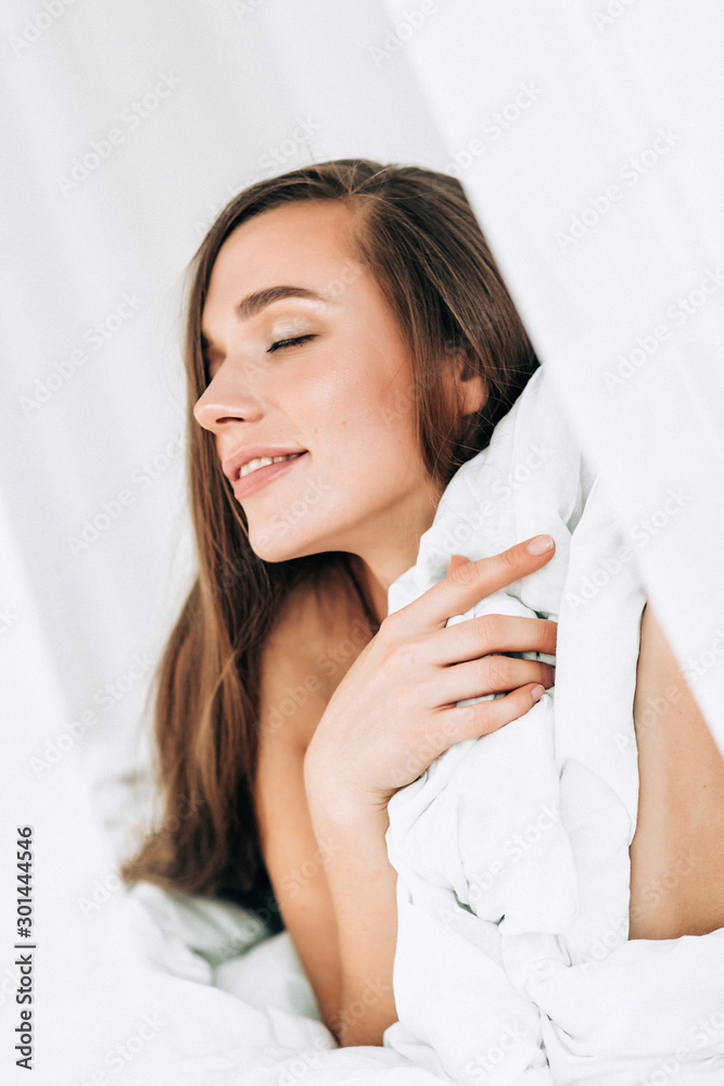 A young beautiful woman with long hair wakes up on the white bed at home, A young beautiful woman with long hair wakes up on the white bed at home,