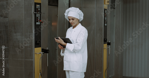 Mature woman , checking the industrial oven machine take some notes on the tablet