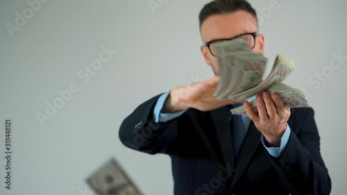 Formally dressed man scatters dollar bills around him, making money rain