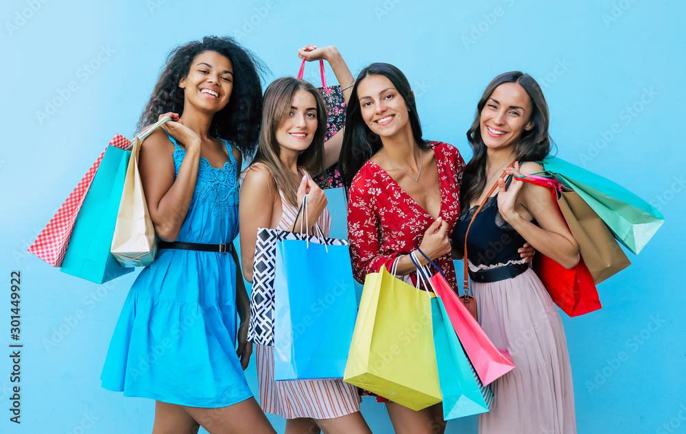 True women. Close up photo of four female friends, posing together in multicolored outfits, holding shopping bags, smiling and looking in the camera. True women. Close up photo of four female friends, posing together in multicolored outfits, holding shopping bags, smiling and looking in the camera.