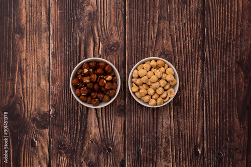 Roasted and raw hazelnuts in bowls on wood background. Healthy snacks.