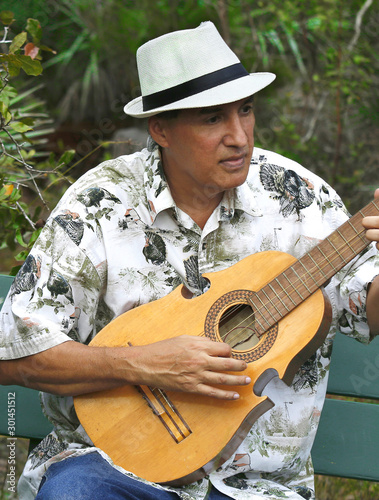 Photography Man with white traditional hat playing a puerto rican cuatro guitar in the field