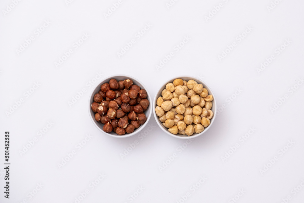 Raw and roasted hazelnuts on white background. Isolated hazelnuts in a bowl. Raw and roasted hazelnuts on white background. Isolated hazelnuts in a bowl.