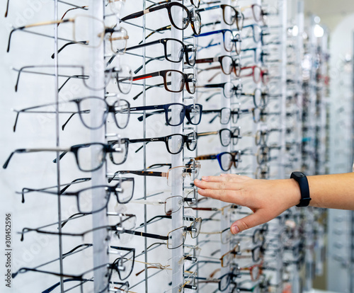 Row of glasses at an opticians. Eyeglasses shop. Stand with glasses in the store of optics. Woman's hand showes glasses. Presenting spectacles. © Vadim