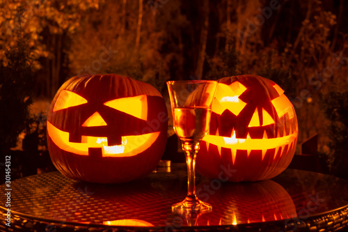 Carved pumpkins - a lamp at night on the table, Halloween decoration, a glass of prosecco, Halloween celebration