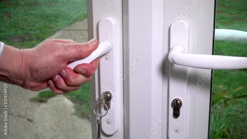 Slow motion close POV close shot of a man’s hands closing a glass conservatory / patio door leading out to a garden / yard, then lifting the handle and using a key to lock the door. photo