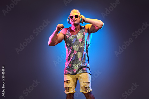 Fashion Charismatic DJ man in Stylish headphones with trendy hairstyle dance in neon creative light. Nightlife club, EDM house music concept. Handsome sexy muscular guy enjoy music dancing