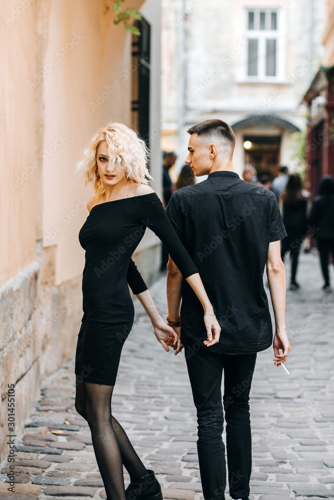 Luxury couple walking down the street holding hands. Gorgeous blonde woman looking back