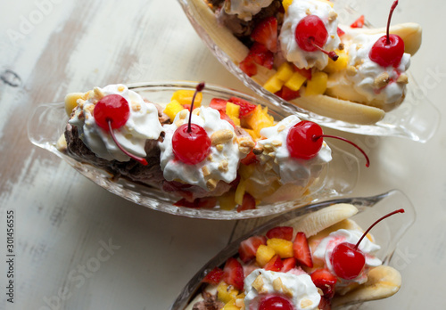 Close up of three banana splits with fresh fruit topping and whipped cream with maraschino cherries.  photo