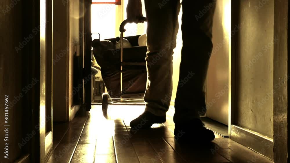 Backlit POV shot at ground level in strong sunlight, of a man pulling a laden shopping trolley up a step and along the floor into his home. Backlit POV shot at ground level in strong sunlight, of a man pulling a laden shopping trolley up a step and along the floor into his home.