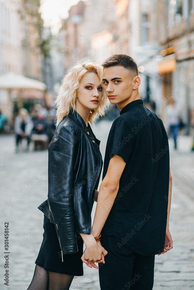 Stylish couple in black clothes posing outdoors holding hands looking back