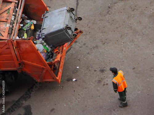 Municipal service garbage disposal, a worker in orange jacket throws a garbage can into a garbage truck
