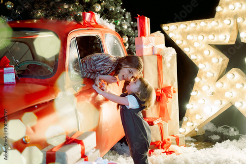 Two sisters in a christmas photo studio. Cute baby girl in a fashionable pin-up dress. many lights and garlands on the Christmas tree. Red retro car. Family celebration. Christmas holiday concept. photo