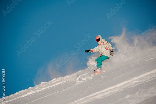 Woman snowboarder riding down the hill in the background of clear sky photo