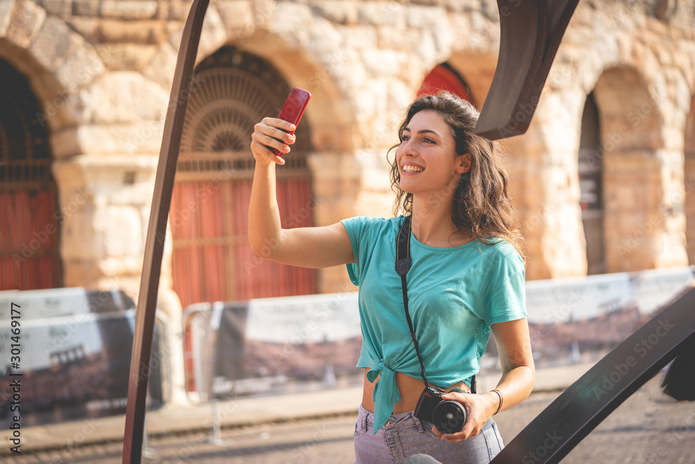 Girl tourist on holiday in Verona taking a selfie, Italy, in front of the arena of Verona before the opera - obrazy, fototapety, plakaty 