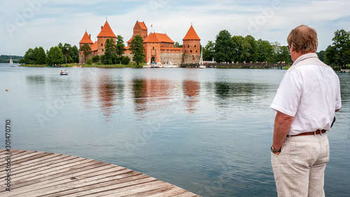 A Mature man looks at an ancient castle on an island. Trakai castle photo