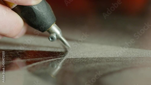 Closeup view of worker's hand carefully making sandblasting writing as kind of engraving on dark surface of granite block dedicated for memorial stone, headstone or grave marker. photo