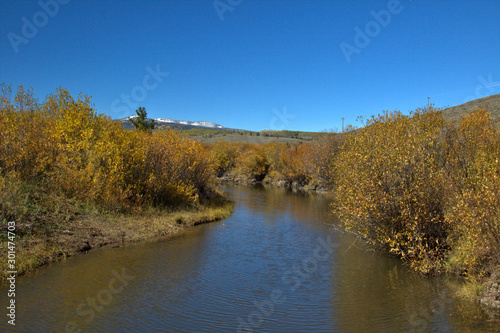 Mountain stream flowing between the fall colors along the stream with snow covered peaks in the background