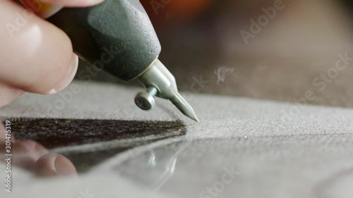 View of worker's hand carefully making sandblasting writing as kind of engraving on dark surface of granite block dedicated for memorial stone, headstone or grave marker.