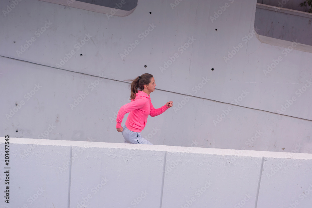 Young female runner in hoody is jogging in the city street.Fit body requires hard work. Urban sport concept. Young female exercising in sport clothes. Young female runner in hoody is jogging in the city street.Fit body requires hard work. Urban sport concept. Young female exercising in sport clothes.