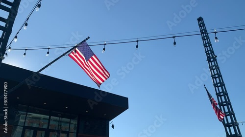 An American flag steadily blowing in the wind while sitting atop a silhouetted structure on a pier. A string of lights cuts across the frame photo